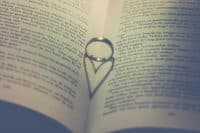 A wedding ring balanced between pages of a book casting a heart-shaped shadow