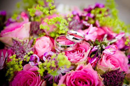 A photo of a pink and green wedding bouquet with two wedding rings on top
