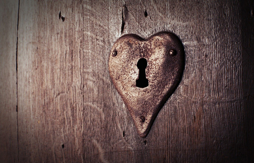 A lock in the shape of a heart rusts away on an old wooden door.