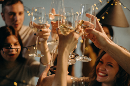 A group of friends celebrates with a newly engaged couple, toasting with champagne.