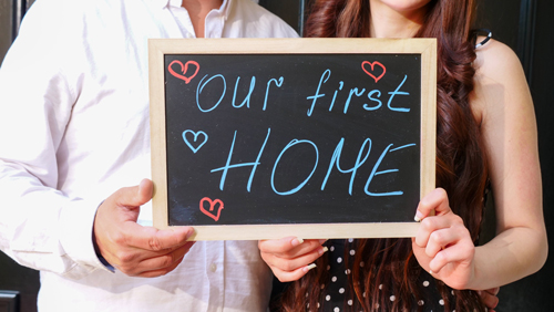 A concept shot of a young couple holding up a sign stating Our First Home.